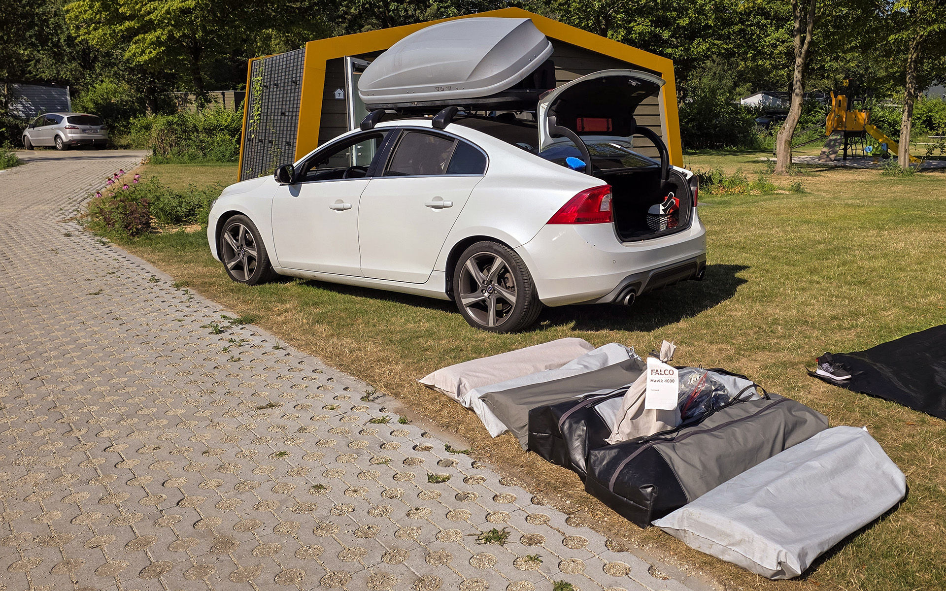 Volvo S60 met geopende kofferbak en dakkoffer, met de ingepakte Falco Havik 4600 en tentzakken klaar om in te laden